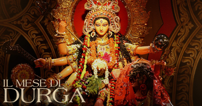 una statua colorata e decorata di Duraga con tante braccia sul leone e la scritta Il mese di Durga