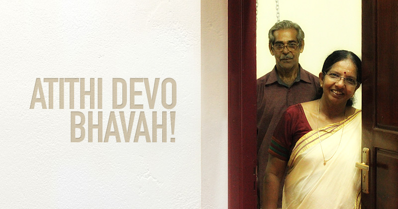 sulla porta di casa una coppia di indiani guardano verso l'esterno, a sinistra la scritta su muro bianco Atithi devo bhavah!