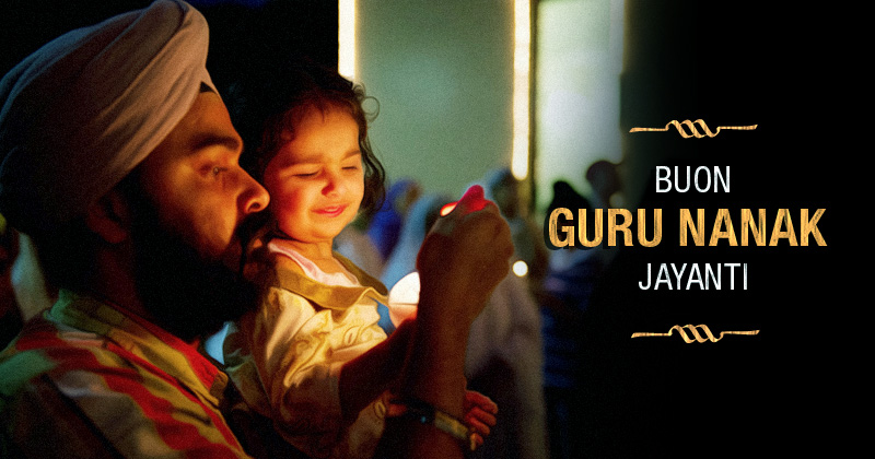 un padre sikh tiene in braccio una bimba e ha un lumino in mano, a sinistra la scritta: buon guru nanak jayanti