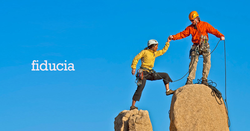 Un ragazzo aiuta una scalatrice a salire in cima a un picco roccioso